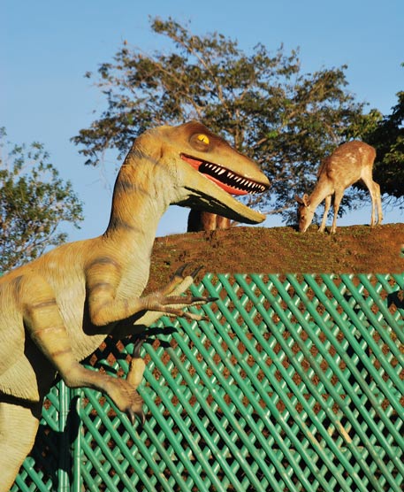 Dinosaur statue. From this perspective, it looks real and as if it's going to eat the live deer on a hill.