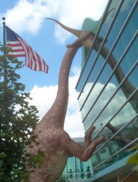 A huge dinosaur rears up the front of the museum while a smaller one is making its entry.