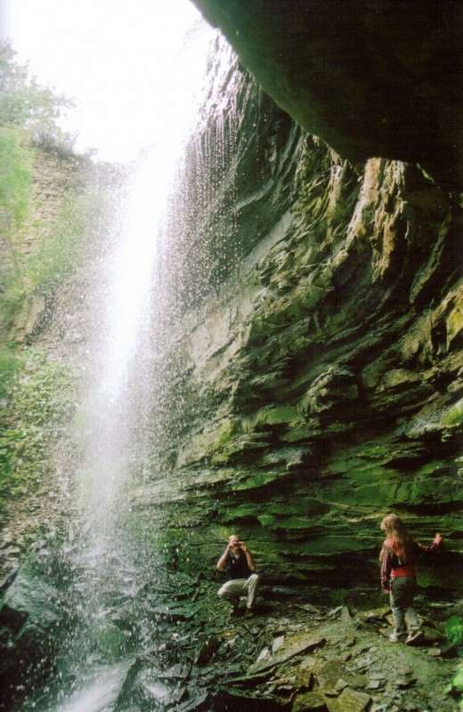 Behind Buttermilk Falls. A person is taking a picture of a girl who also is behind the falls (and dry).