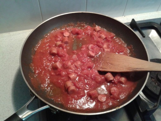 Adding the chopped tomatoes to the garlic and hotdogs.