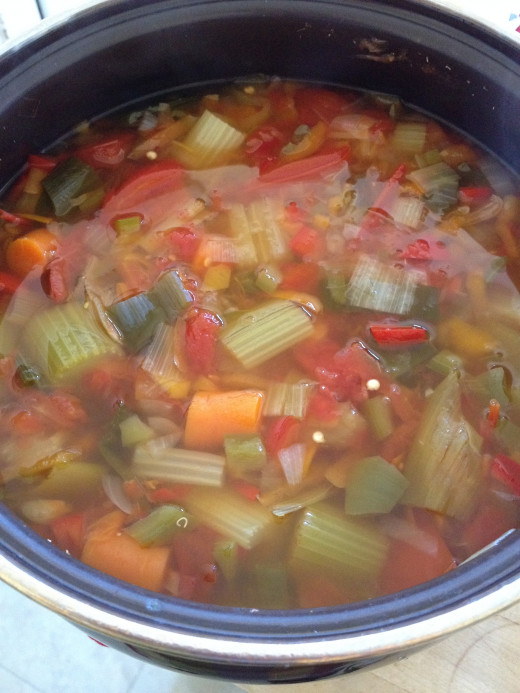 A pot of tomato-vegetable soup stock just coming to the boil on top of the stove