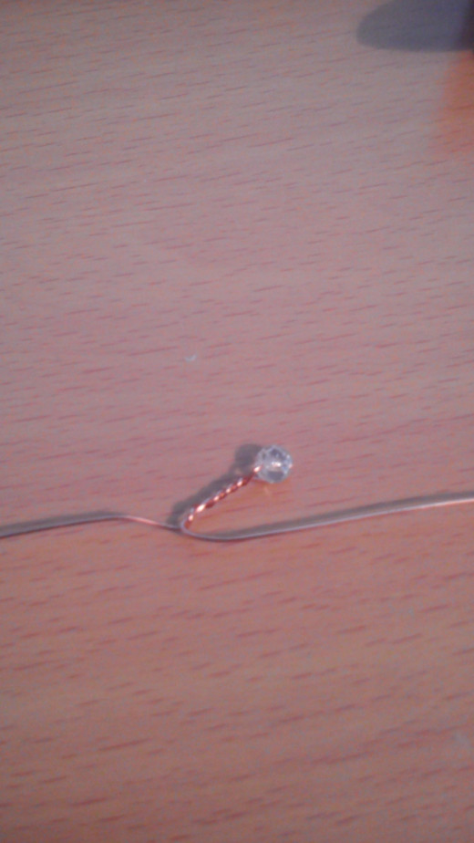 Thread a bead to approx 10cm along the length of wire, hold in place, bend one end back around to meet the other, now still holding the bead in place rotate the hand holding the bead so that the wire twists together to about 1cm under the bead.