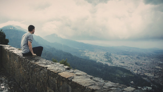A man sitting on a wall overlooking a city.