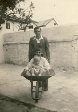 Dad pushing me (in front) and Chris in a wheelbarrow at the back of Aunt Queenie's house