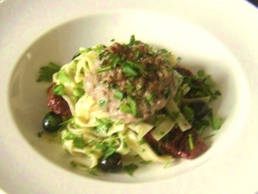 Lamb burger served on a bed of tagliatelle pasta, sun dried tomatoes and black olives