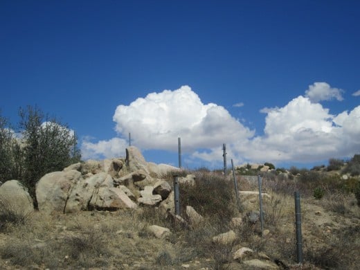 Clouds floating in the sky with a fence along the hillside.