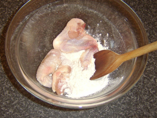 Chicken wings are tossed in seasoned flour for deep frying