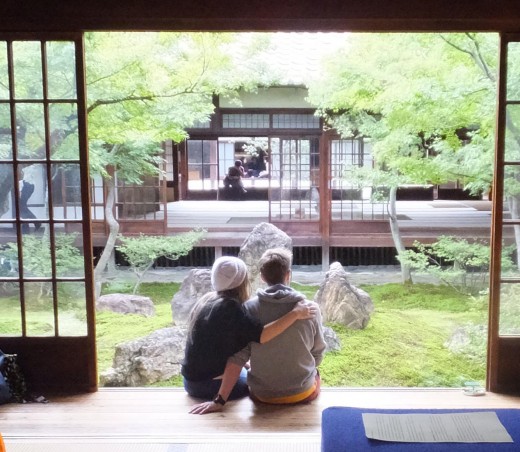 Two people, one with the arm around the other, sitting in a doorway overlooking a garden in Japan.