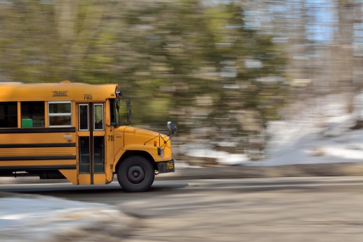 Image of the front part of a school bus driving on a road with a blurry background.