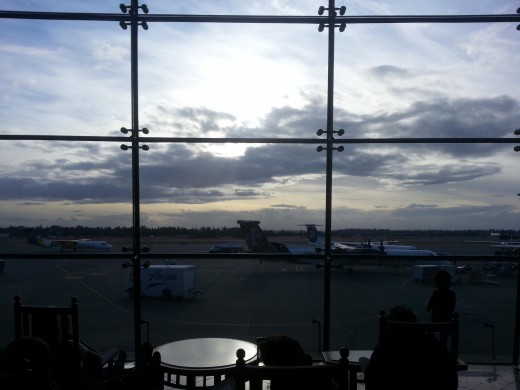 Image of a plane outside of an airport, framed by a window, with the sun nearly covered by clouds.