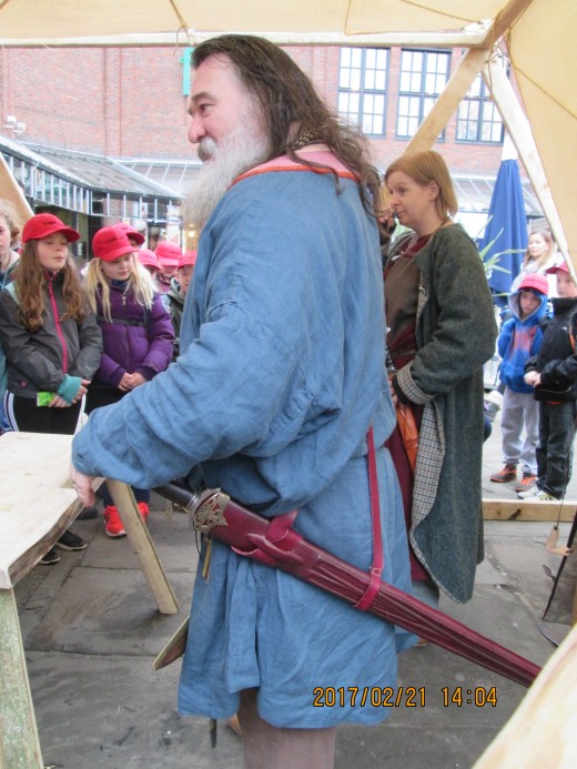 Meet the Jarl, Norse equivalent of Earl, as he engages a youthful audience to inform them of a re-enactment. The girl behind him, from Glasgow, has taken on the guise of a woman skald. Not just men travelled between settlements with sagas to tell