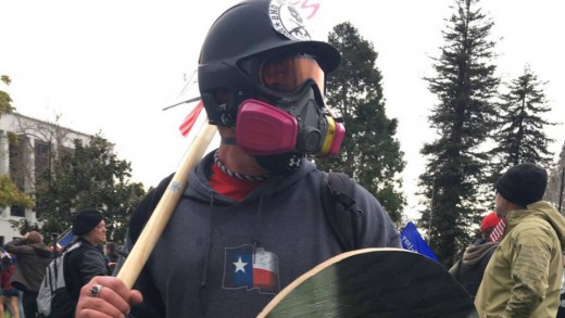 Based Stick Man donning his signature stick at a rally, as well as a helmet, gas mask and shield.