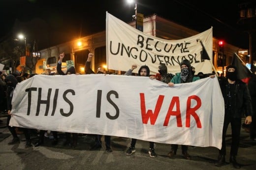 Antifa and Black Bloc holding signs saying "Become Ungovernable" and "This Is War".