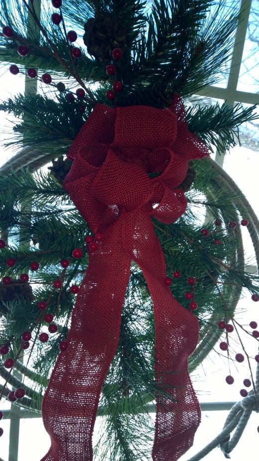 Photo shows closeup of western-style Christmas Wreath hung on a window. Snowy fields in the background.