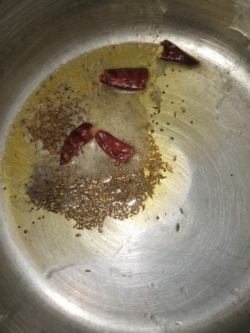 In a cooker heat butter and oil, add mustard seeds and cumin seeds, let it splutter, add dry red chilies, fry.