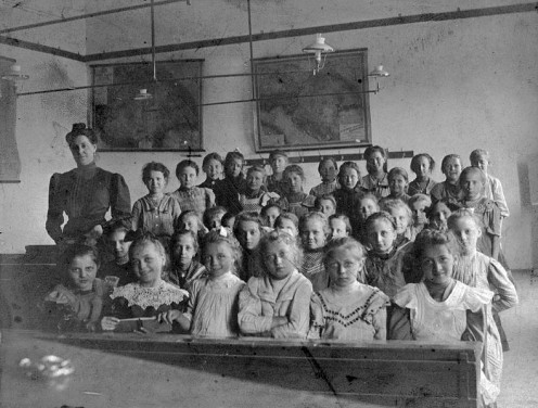 1908 classroom with teacher and children all sitting still and showing respect.