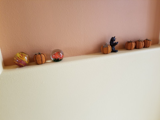 On this narrow wall ledge, I used small wrapped pumpkins and mingled them with some orange paperweights. The cat figurine accents the other items.