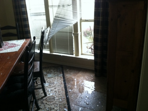 Before  repairs.  Dining room and windows hail damage. Note the broken glass on the floor, water and blinds being blown back.