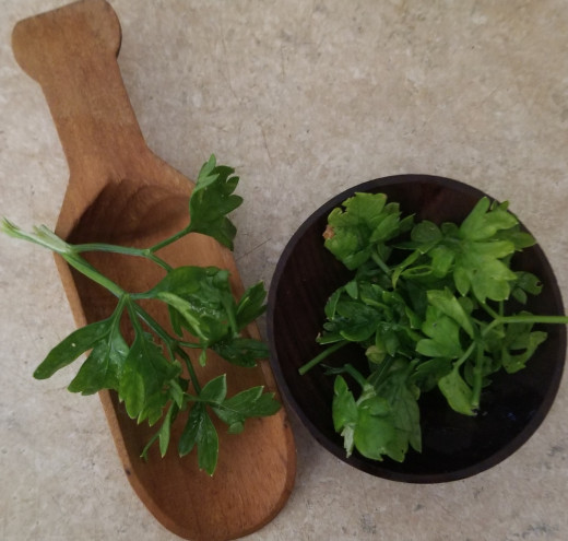 Parsley in small wooden bowl and spoon, ready to add to a plate of food as a garnish.