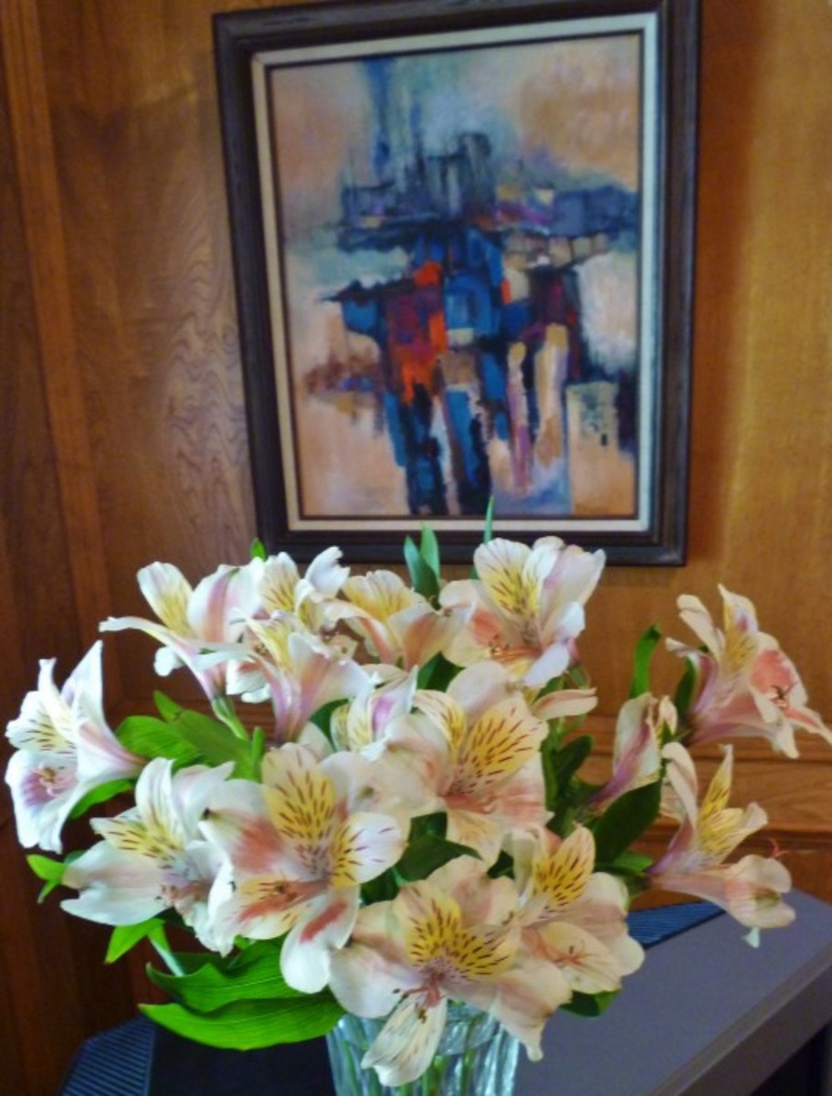 A Dr. Robert Rogan painting is on the wall behind a vase of pink blush alstroemeria flowers. A Dr. Robert Rogan painting is on the wall behind a vase of alstroemeria flowers.