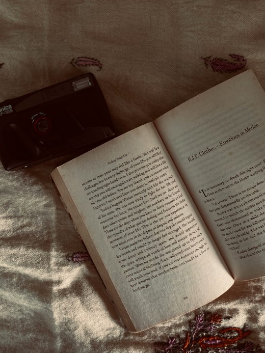 An open book sitting on top of a bed next to a camera, Photo by Alan Girish on Unsplash