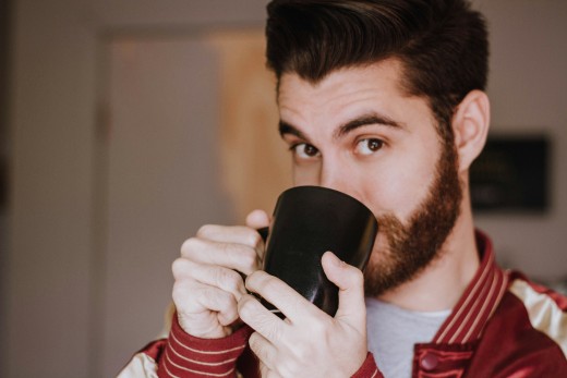 A man with a beard holding a coffee mug, 