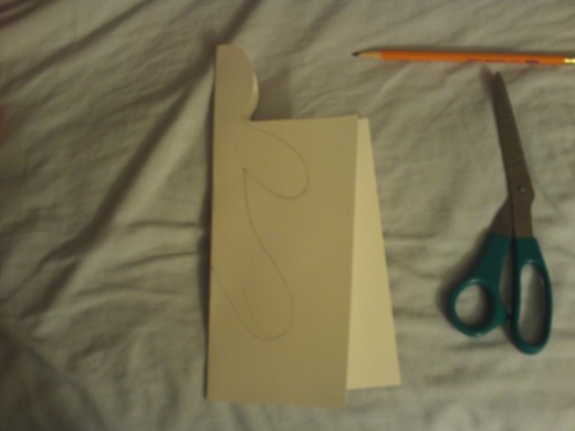 Fold the card stock in half, and make sure the half head is equal on both sides.  Use the scissors to even out if it is not.  Next, draw half of the gingerbread boy's body onto the card stock.  Cut the figure out of the card stock.