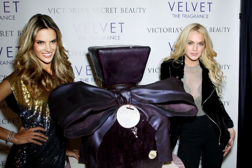 Lindsay Lohan pokes a hole into VS Velvet's perfume cake with her hand as press watches on.