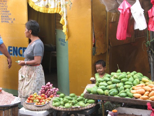 A vendor selling mangos and tomatoes as her son takes a snack.