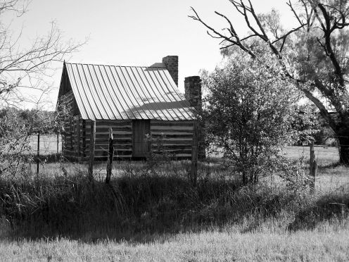 Black and White photo of a rare, double chimney log cabin that has been restored. Very rare to see one with two chimneys!