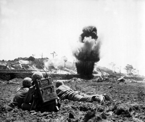 A 6th Division Marine demolition crew watches explosive charges detonate and destroy a Japanese cave, May 1945.