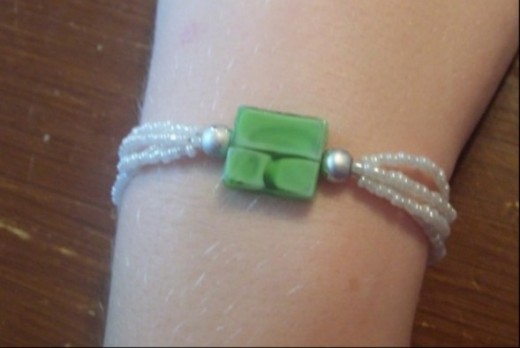Multi-strand bracelet made with four strands. The three focal beads are then strung onto all four strands in the middle and the piece is finished out with the four strands separated again. 