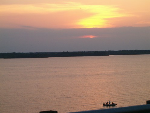Fishermen in a little boat, enjoying a lake at sunset.