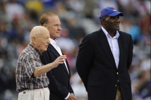 Nicolas Baldino, left, waves to the crowd after being honored by Frank Gifford, center, and Harry Carson, right, as a season ticket-holder since the 1940s in all four stadiums that the New York Giants have called home, during halftime of an NFL footb