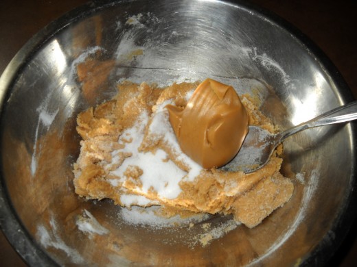 Peanut butter and sugar in the mixing bowl being blended to create a smooth dough.