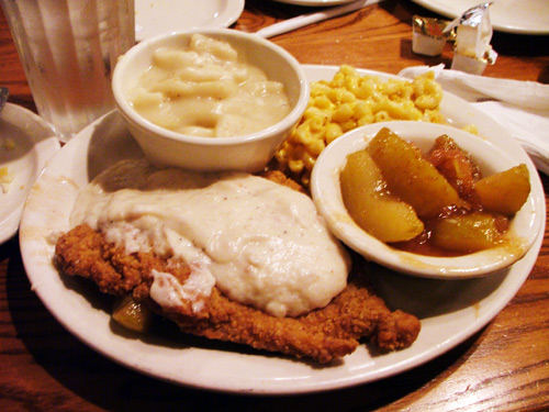 A plate of Cracker Barrel chicken with their delicious gravy, mashed potatoes, mac n' cheese and apple slices.