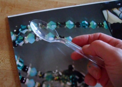 Use a plastic spoon to smooth the glued picture down on the cardboard.