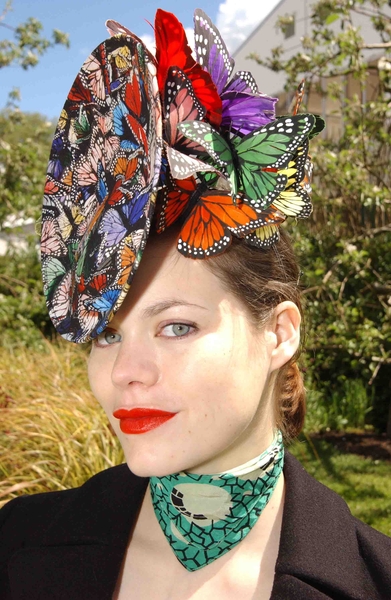 A clutch of colourful butterflies resting on a models head. Hat by Philip Treacy