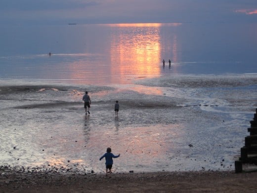 Children messing about on the shore as the sun goes down.