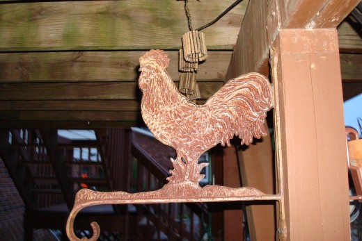 Rusty Wrought Iron Rooster Plant Hanger is hanging over the Garden