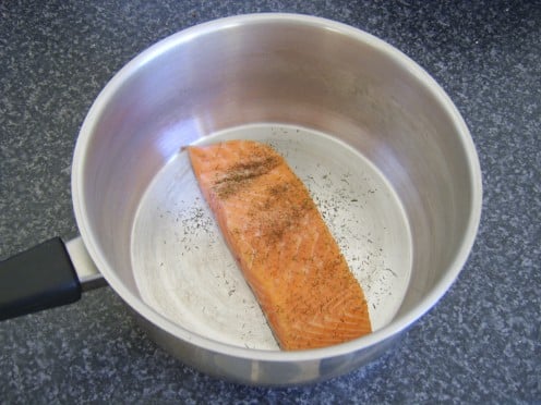 Salmon fillet is laid skin side down in a pot and seasoned with salt, white pepper and dried dill