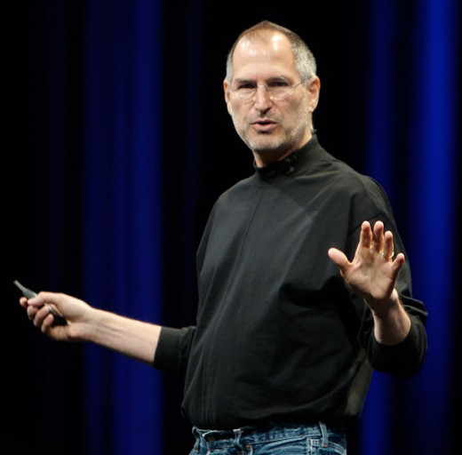 Steve Jobs speaking at one of his conferences with his famous look - black turtleneck  shirt and jeans.