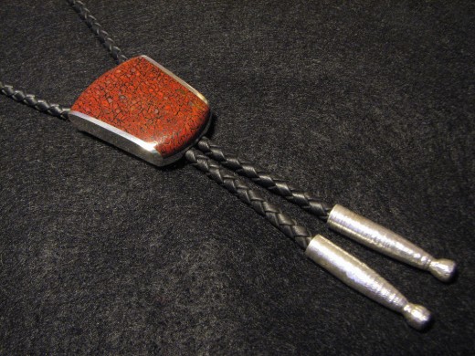 A very traditional bolo tie made with braided leather. Note the sterling silver aguillettes and dinosaur bone inlay on the decorative slide.