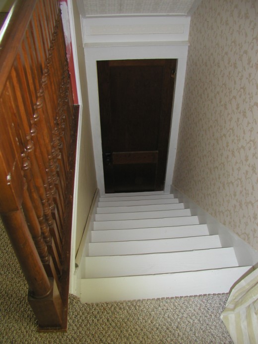 back stairway leading to door which goes to another landing and then, several steps lower; the kitchen