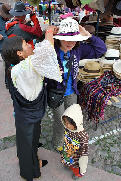 An Otavalo woman helps a tourists try on a hat.