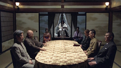 At the table are the six men hunting Izo.  Before then is the god-like emperor, the woman and man to his side wear traditional garb.