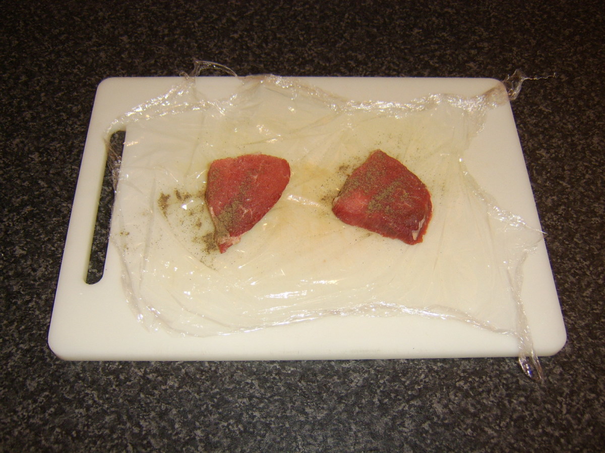 Steak is seasoned and enclosed between two sheets of plastic wrap for pounding