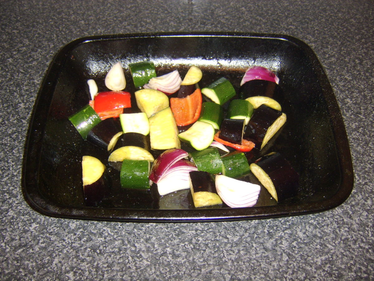 Olive oil and seasoning is added to the vegetables in a roasting tray