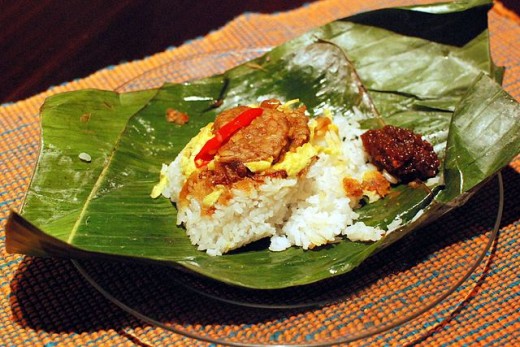 Indonesian Nasi uduk (rice cooked in coconut milk) comes wrapped in banana leaf and featured fried tempeh (soya bean cake), omelet, seasoned and roasted coconut flakes), and peanuts.