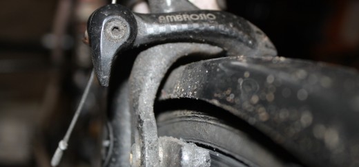 A circular cam on a (dirty) road bike caliper lifts up to increase clearance between the tyre/ rim and brake pads